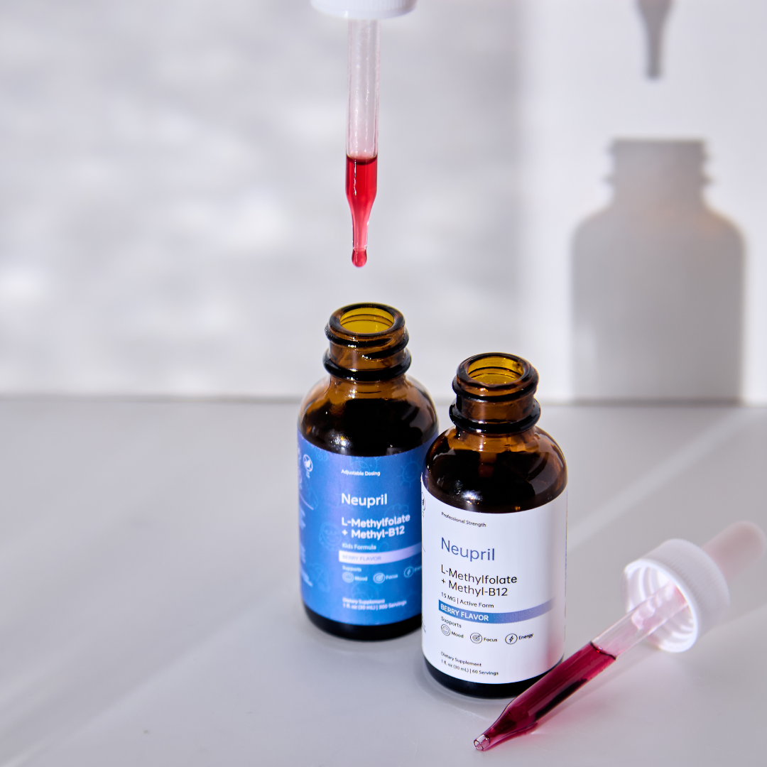 A top-down shot of two Neupril L-Methylfolate + Methyl-B12 bottles with glass droppers. A dropper suspended above an open bottle releases a vibrant red, berry-flavored liquid drop. The background is a clean white with soft, artistic shadows, highlighting the supplement's clarity and natural color.