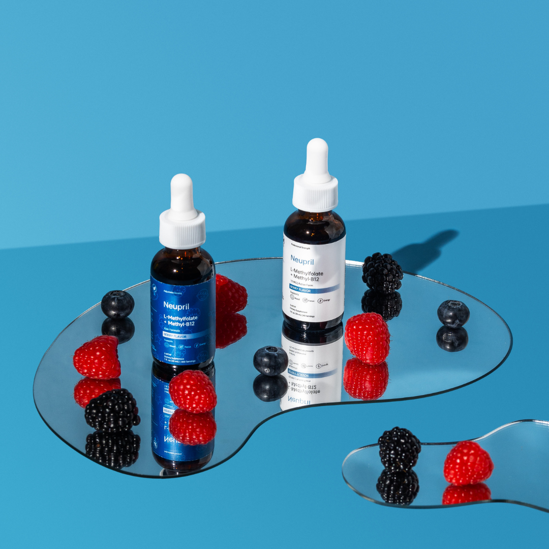 Two Neupril L-Methylfolate + Methyl-B12 dropper bottles—one blue Kids Formula and one white Professional Strength—standing on organic-shaped mirrors. Fresh raspberries, blackberries, and blueberries are scattered around the bottles, creating vibrant reflections on a bright blue background